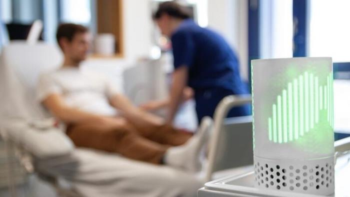 The Resmonics sensor glowing green on a hospital ward, a nurse and a patient behind it